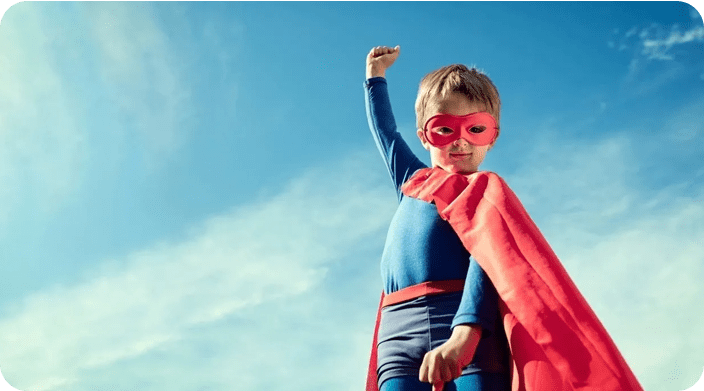 A young boy dressed as superman with a red cape and mask.