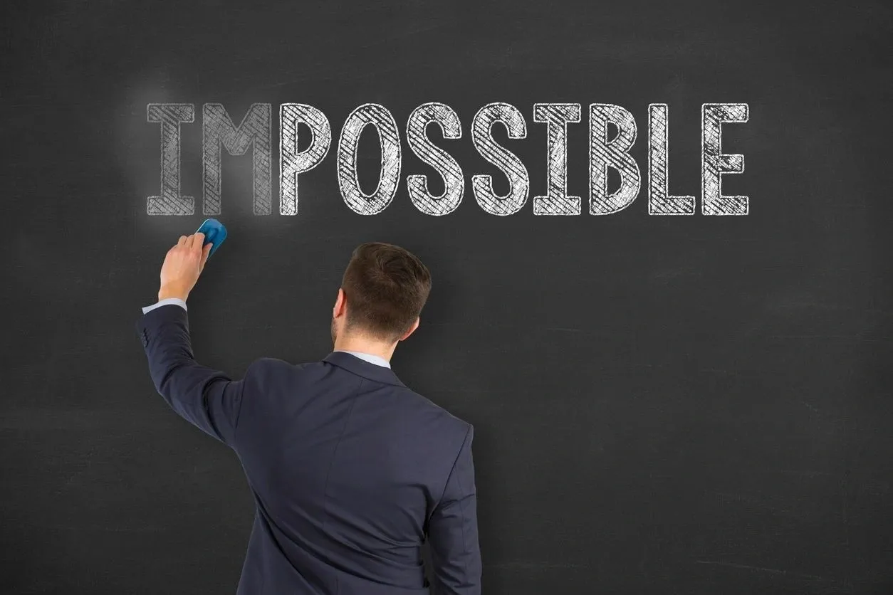 A man writing the word impossible on a chalkboard.